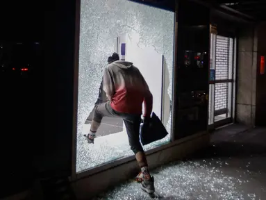 Seorang pendemo memasuki toko melalui jendela yang rusak di New York, AS (1/6/2020). Sejumlah toko di Amerika Serikat dijarah oleh pendemo yhang mengecam kematian warga kulit hitam George Floyd. (Foto AP / Frank Franklin II)