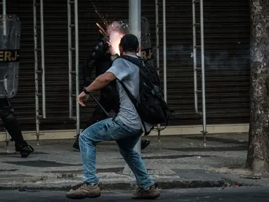 Pengunjuk rasa melemparkan petasan ke arah polisi saat bentrokan memprotes rencana pembatasan belanja publik di Rio de Janeiro, Brasil, (9/2). (AFP Photo / Yasuyoshi Chiba)