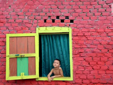 Seorang bocah melongok keluar jendela di Kampung Warna Warni Lubuklinggau, Sumatera Selatan, Rabu (10/1). Kampung yang dulunya menjadi pusat perjudian, sabung ayam, dan lokasi transaksi narkoba itu kini telah berubah wajah (Liputan6.com/Immanuel Antonius)