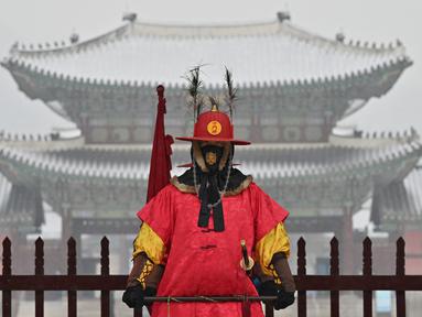 Seorang 'penjaga istana' berdiri untuk turis di depan Istana Gyeongbokgung yang tertutup salju di pusat kota Seoul (19/1/2022). Pihak berwenang di Seoul dan daerah sekitarnya pada Rabu (19/1) tetap waspada karena wilayah ibu kota diperkirakan akan turun salju lebat sepanjang hari. (AFP/Jung Yeon-je)