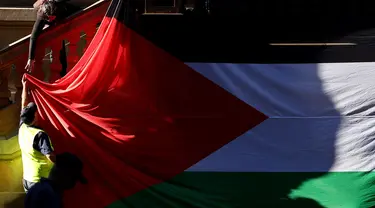 Para pengunjuk rasa menggantungkan bendera Palestina berukuran besar di dinding Balai Kota pada awal unjuk rasa menentang aksi militer Israel di Gaza saat mereka berkumpul di Sydney pada 9 Oktober 2023. (David GRAY/AFP)