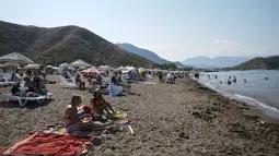 Orang-orang berjemur saat menikmati cuaca cerah, laut dan matahari, sehari sebelum jam malam hari Minggu di Adrasan, 100 kilometer barat Antalya, di Mediterania Turki, Sabtu (19/6/2021).  (AP Photo/Burhan Ozbilici)