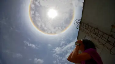 Seorang wanita mengamati fenomena Halo Matahari yang terjadi di atas langit kota Caracas, ibu kota Venezuela, 10 Mei 2016. Fenomena langka itu dinamakan Halo Matahari yang terbentuk akibat refleksi dari kristal es. (Juan BARRETO/AFP)