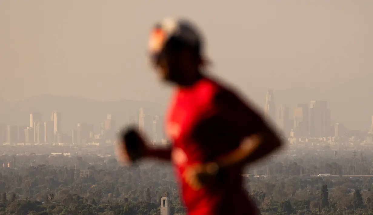 Seorang pelari melintas di depan kabut asap dari berbagai kebakaran hutan di cakrawala pusat kota Los Angeles, Rabu, 11 September 2024. (AP Photo/Etienne Laurent)