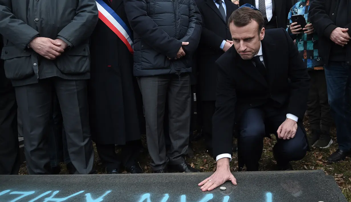 Presiden Prancis Emmanuel Macron meletakkan batu di atas makam Yahudi yang dicoret simbol Nazi di pemakaman Yahudi, Quatzenheim, Prancis, Selasa (19/2). Macron juga juga menyatakan akan menghukum para pelaku vandalisme. (Frederick FLORIN/AFP)