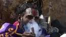 Seorang Sadhu atau orang suci Hindu menghisap ganja menjelang festival Hindu 'Maha Shivaratri', di Kathmandu (9/3/2021). Ratusan orang suci datang ke kuil untuk mengisap ganja, mereka dapat merokok ganja (hanya di kuil) dan melaburi tubuhnya dengan abu. (AFP/Prakash Mathema)