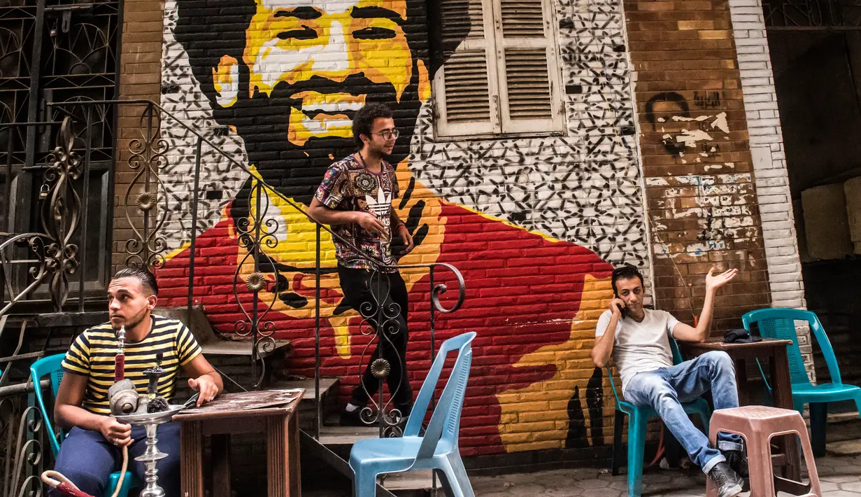 Ahmed Fathy (tengah) menuruni tangga dekat mural bintang Liverpool, Mohamed Salah di sebuah kedai kopi di pusat kota Kairo, 30 April 2018. Mural pemain timnas Mesir tersebut merupakan hasil karya Fathy. (AFP Photo/KHALED DESOUKI)