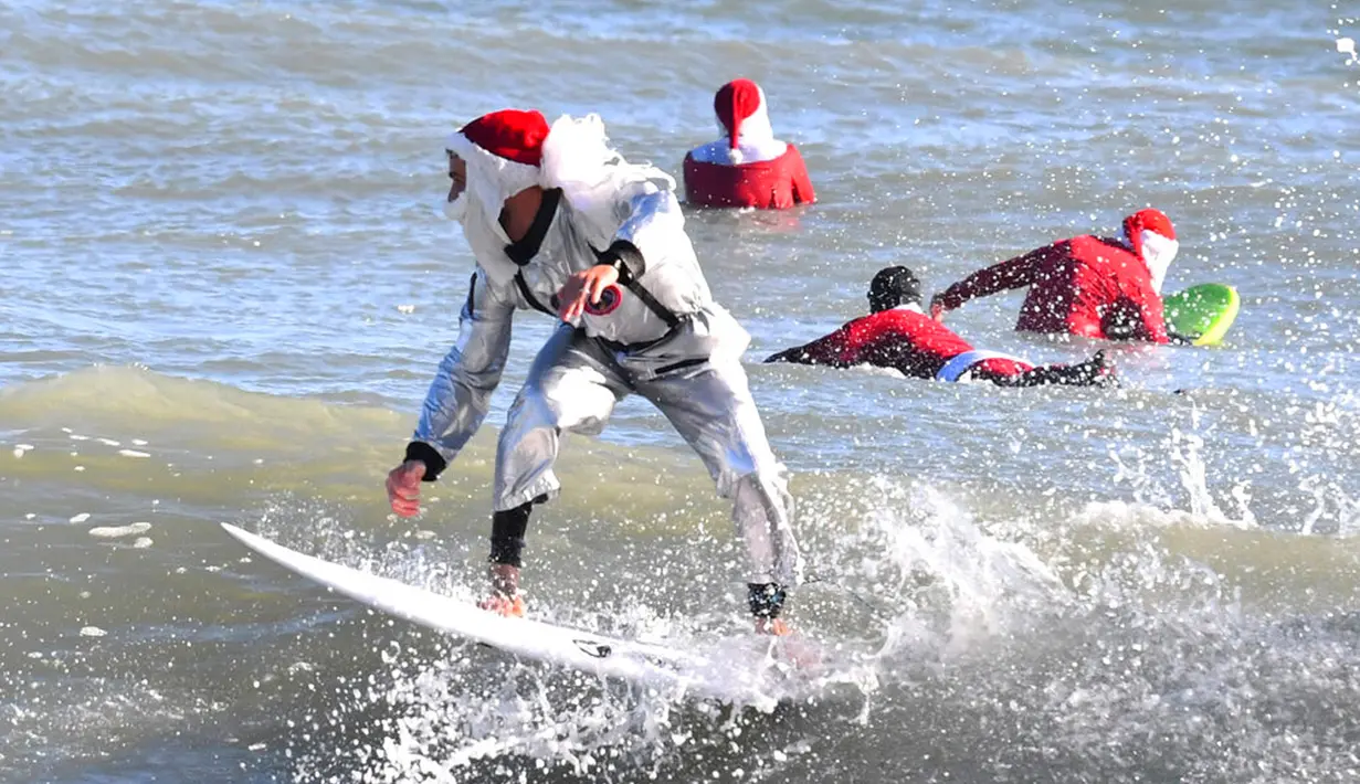 Peselancar Corey Howell yang menganakan pakaian luar angkasa serta Sinterklas berselancar untuk acara tahunan ke-14 Surfing Santas of Cocoa Beach di Cocoa Beach, Florida, Amerika Serikat, 24 Desember 2022. (Malcolm Denemark/Florida Today via AP)