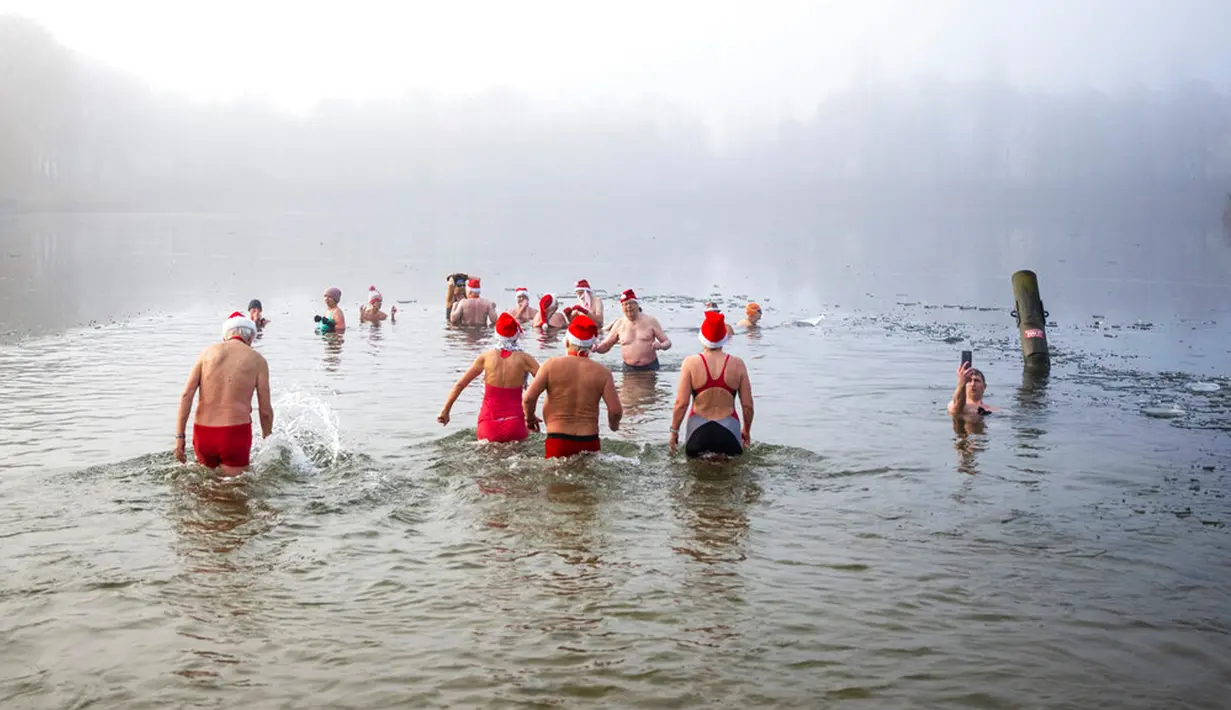 Tiga anggota asosiasi "Berliner Seehunde" berenang di antara bongkahan es saat mandi Natal di Danau Orankesee, Berlin, Jerman, Minggu (25/12/2022). (Christophe Gateau/dpa via AP)