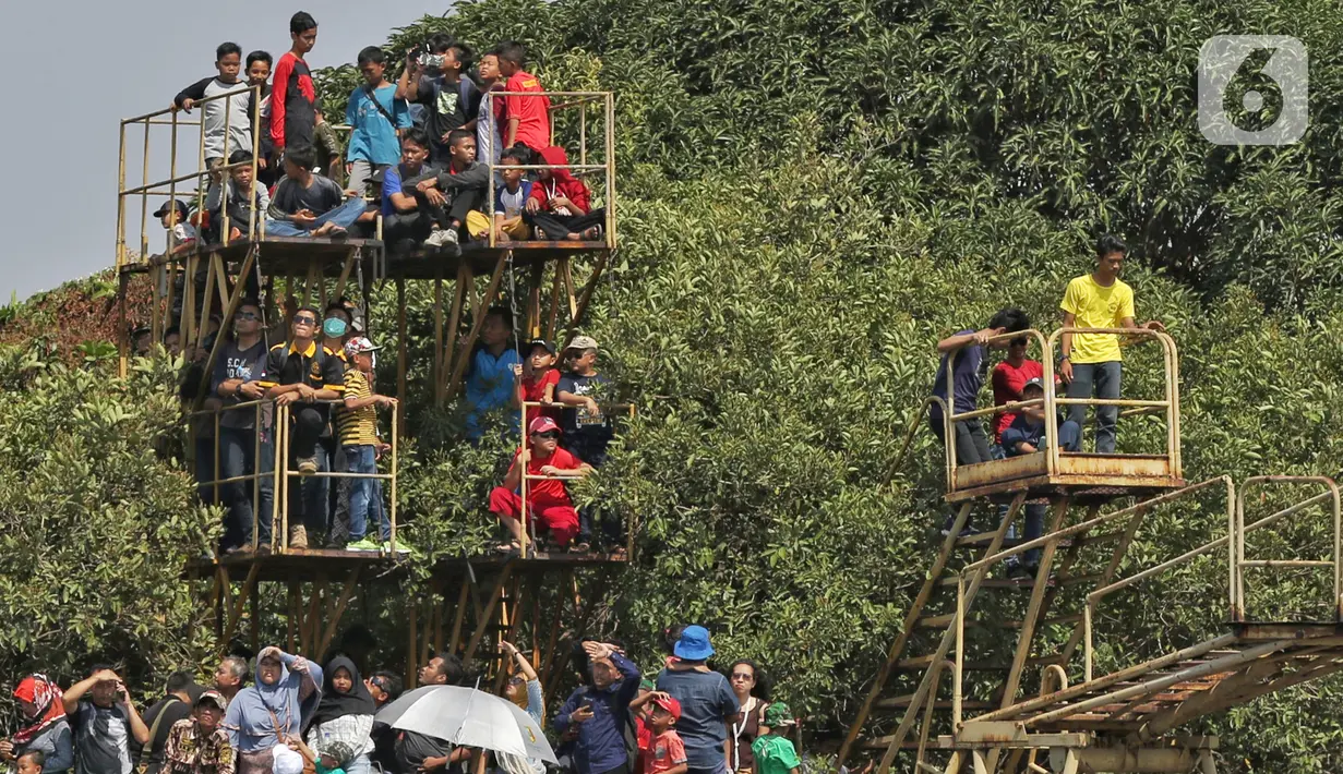Sejumlah warga menaiki bangunan besi saat menyaksikan perayaan HUT ke-74 TNI di Lanud Halim Perdanakusuma, Jakarta Timur, Sabtu (5/10/2019). Warga rela panas-panasan dan berdesak-desakan untuk menyaksikan perayaan HUT ke-74 TNI. (Liputan6.com/JohanTallo)
