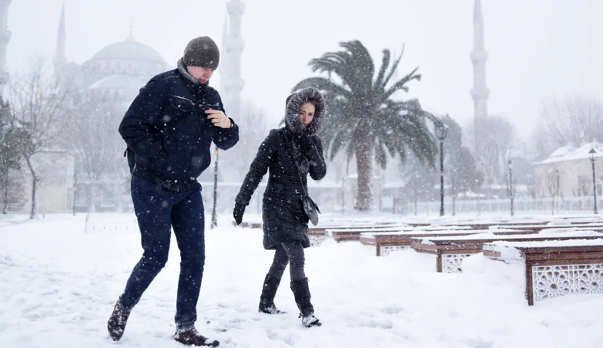 Sepasang warga berjalan menembus timbunan salju di tengah badai di kawasan Sultanahmet, distrik wisata bersejarah di Istanbul, Sabtu (7/1). Badai salju dahsyat melumpuhkan Kota Istanbul. (Mert Akyol/Depo Photos via AP)
