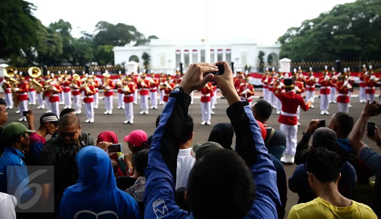 Warga mengabadikan gambar prosesi serah terima pergantian pasukan jaga Istana Kepresiden di depan Istana Merdeka, Minggu (28/8). Ini merupakan pelaksanaan seremoni pergantian pasukan jaga istana untuk yang kedua kalinya (Liputan6.com/Faizal Fanani)