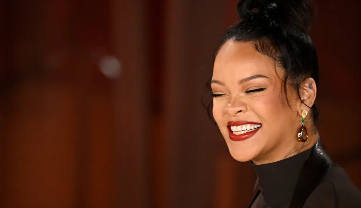 Senyum Rihanna saat menghadiri Academy Awards ke-95 atau Oscar 2023 di Teater Dolby di Hollywood, California pada Minggu, 12 Maret 2023, waktu setempat. Rihanna menata rambutnya dengan high top knot bun dengan untaian rambut yang menjuntai. (Photo by Robyn BECK / AFP)