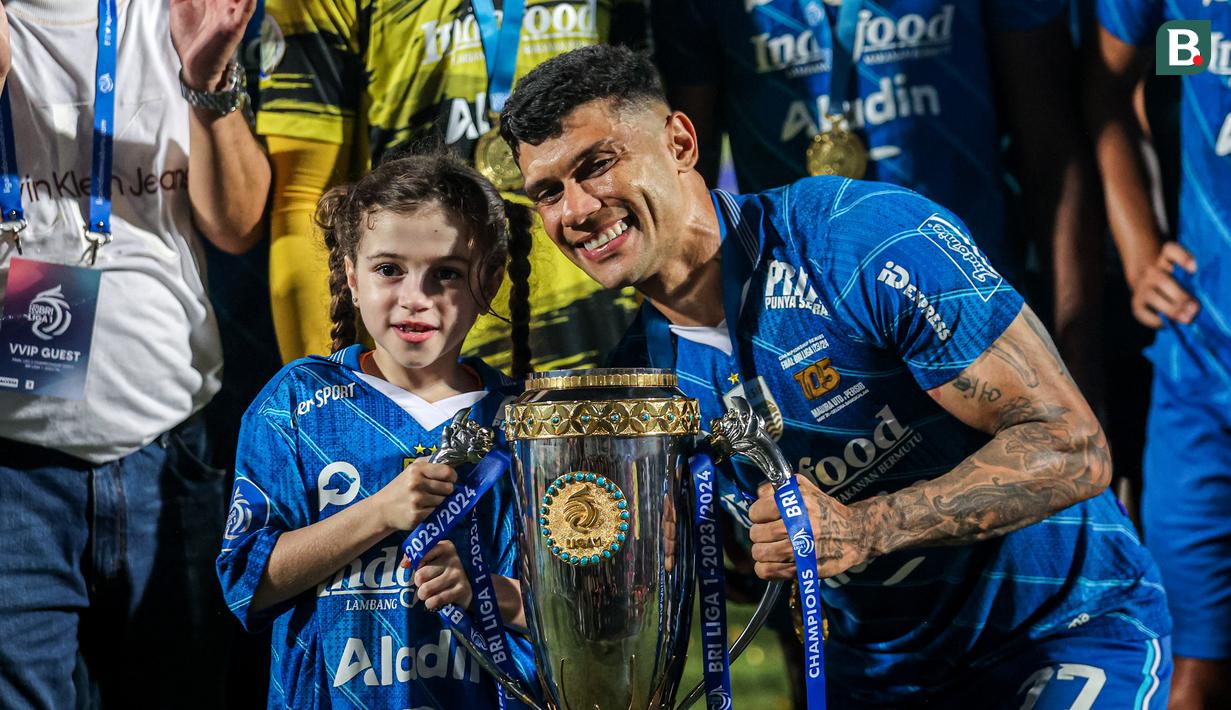 Selebrasi striker Persib Bandung, Ciro Alves dengan trofi juara bersama sang putri, Bella dalam perayaan gelar juara Championship Series BRI Liga 1 2023/2024 setelah mengalahkan Madura United 3-1 pada laga final leg kedua di Stadion Gelora Bangkalan, Madura, Jumat (31/5/2024). (Bola.com/Bagaskara Lazuardi)