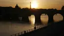 Seorang pria berjalan di tepi sungai Seine dengan latar belakang Menara Eiffel, saat matahari terbenam, di Paris (29/3/2021). Sungai ini membelah kota Paris menjadi dua bagian yang dalam bahasa Prancis disebut la rive droite ("tepi kanan") dan la rive gauche ("tepi kiri"). (AP Photo/Thibault Camus)