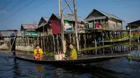 Masyarakat melewati rumah-rumah panggung menggunakan perahu di kampung terapung Danau Inle, Negara Bagian Shan, Myanmar, Senin (18/2). Seluruh kehidupan warga praktis berhubungan dengan perairan Danau Inle. (Ye Aung THU/AFP)