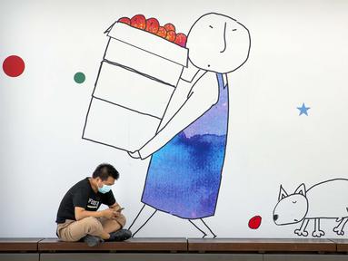Seorang pria yang memakai masker untuk melindungi dari virus corona COVID-19 duduk di depan mural kompleks perbelanjaan dan perkantoran, Beijing, China, 11 Agustus 2020. China dan Hong Kong mengalami penurunan kasus COVID-19. (AP Photo/Mark Schiefelbein)
