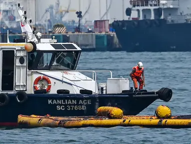 Seorang pekerja pembersihan di atas kapal berdiri di atas alat penyedot minyak selama operasi untuk membersihkan minyak dari tumpahan minyak di dekat terminal pelabuhan Pasir Panjang di Singapura pada tanggal 18 Juni 2024. (ROSLAN RAHMAN/AFP)