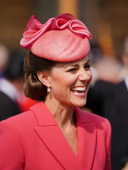 Kate Middleton, Duchess of Cambridge dari Inggris berbicara kepada para tamu di Pesta Taman Kerajaan di Istana Buckingham di London (18/5/2022). Kate Middleton mengenakan gaun mantel koral dengan topi dengan warna yang sama. (AFP/Pool/Dominic Lipinski)