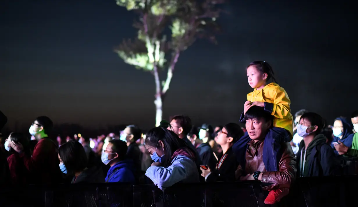Seorang pria menggendong anaknya saat mereka menyaksikan Festival Musik Rye yang digelar selama dua hari di Beijing pada 18 Oktober 2020. (Photo by Noel Celis / AFP)