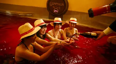 Seorang pria menuangkan anggur ke dalam tangan seorang wanita saat mereka duduk dalam air panas dengan air berwarna anggur di resor spa Hakone Kowaki-en Yunessun saat acara menandai Beaujolais Nouveau Day,Tokyo, Jepang (19/11). (REUTERS/Thomas Peter)