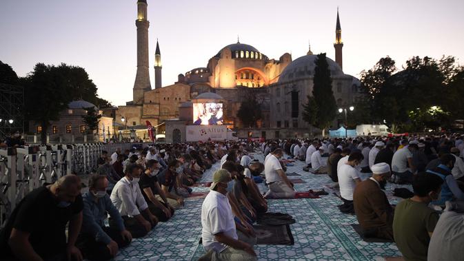 Umat Islam, memanjatkan doa-doa mereka selama salat Idul Adha, dengan latar belakang Hagia Sophia, yang baru-baru ini dikonversi kembali ke masjid, di distrik bersejarah Sultanahmet di Istanbul, 31 Juli 2020.  (AP Photo/Yasin Akgul)