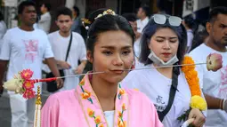 Seorang wanita menusuk pipinya dengan besi  saat mengikuti prosesi perayaan Festival Vegetarian tahunan di Phuket, Thailand, Kamis (3/10/2019). Festival dimulai pada malam pertama bulan lunar kesembilan dan berlangsung selama sembilan hari. (AFP Photo/Mladen Antonov)