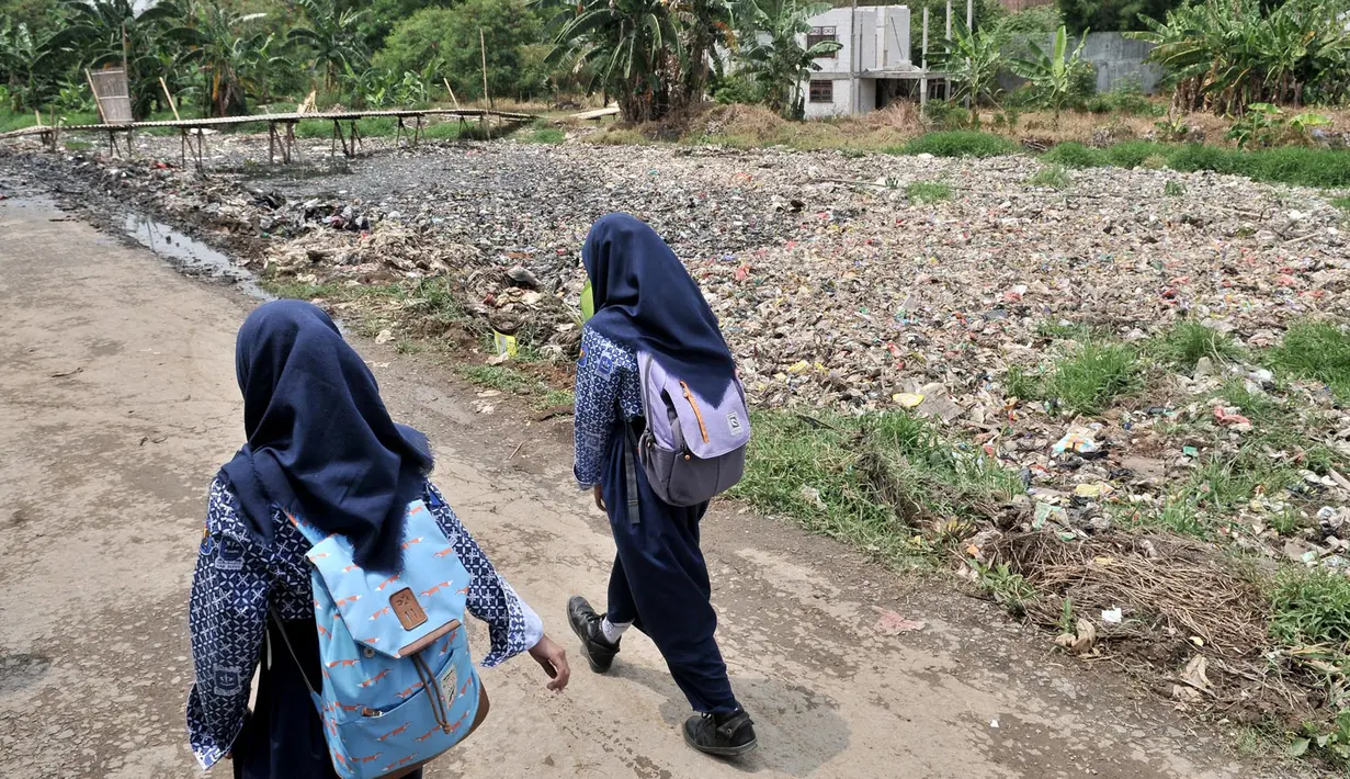 Anak sekolah melintas di pinggir Kali Pisang Batu yang dipenuhi sampah, Tarumajaya, Bekasi, Jawa Barat, Rabu (9/1). Warga tetap beraktivitas meski bau tak sedap menghantui mereka akibat tumpukan sampah di kali tersebut. (Merdeka.com/Iqbal S. Nugroho)