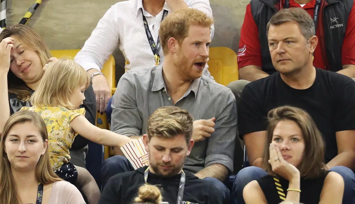 Seorang bocah, Emily Henson diam-diam mengambil popcorn Pangeran Harry yang sedang berbincang dengan rekannya ketika acara Invictus Games di Toronto, Rabu (27/9). Kejadian tertangkap kamera ini begitu menggemaskan. (CHRIS JACKSON/GETTY IMAGES/AFP)