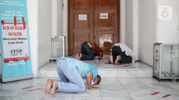 Sejumlah warga melaksanakan salat zuhur di halaman depan Masjid Cut Meutia, Jakarta, Jumat (18/9/2020). Pemprov DKI Jakarta kembali meniadakan kegiatan ibadah salat Jumat dan salat lima waktu berjemaah di semua Masjid Raya selama PSBB. (Liputan6.com/Faizal Fanani)