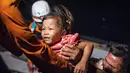 Tim penyelamat membantu anak untuk menaiki kapal saat dievakuasi dari Pulau Sebuku di perairan Selat Sunda (28/12). Ratusan orang tewas dalam Tsunami Selat Sunda yang melanda Sumatera dan Jawa tanpa peringatan akhir pekan lalu. (AP Photo/Fauzy Chaniago)