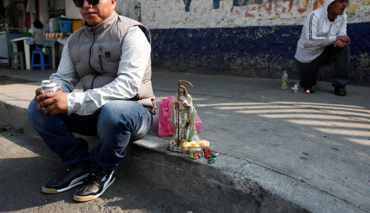 Seorang lelaki duduk dekat patung Santa Muerte saat merayakan tahun baru di Meksiko, Minggu (1/1/2017). Warga Meksiko berkeliling sambil membawa patung Santa Muerte agar memperoleh keberuntungan. (REUTERS/Carlos Jasso)