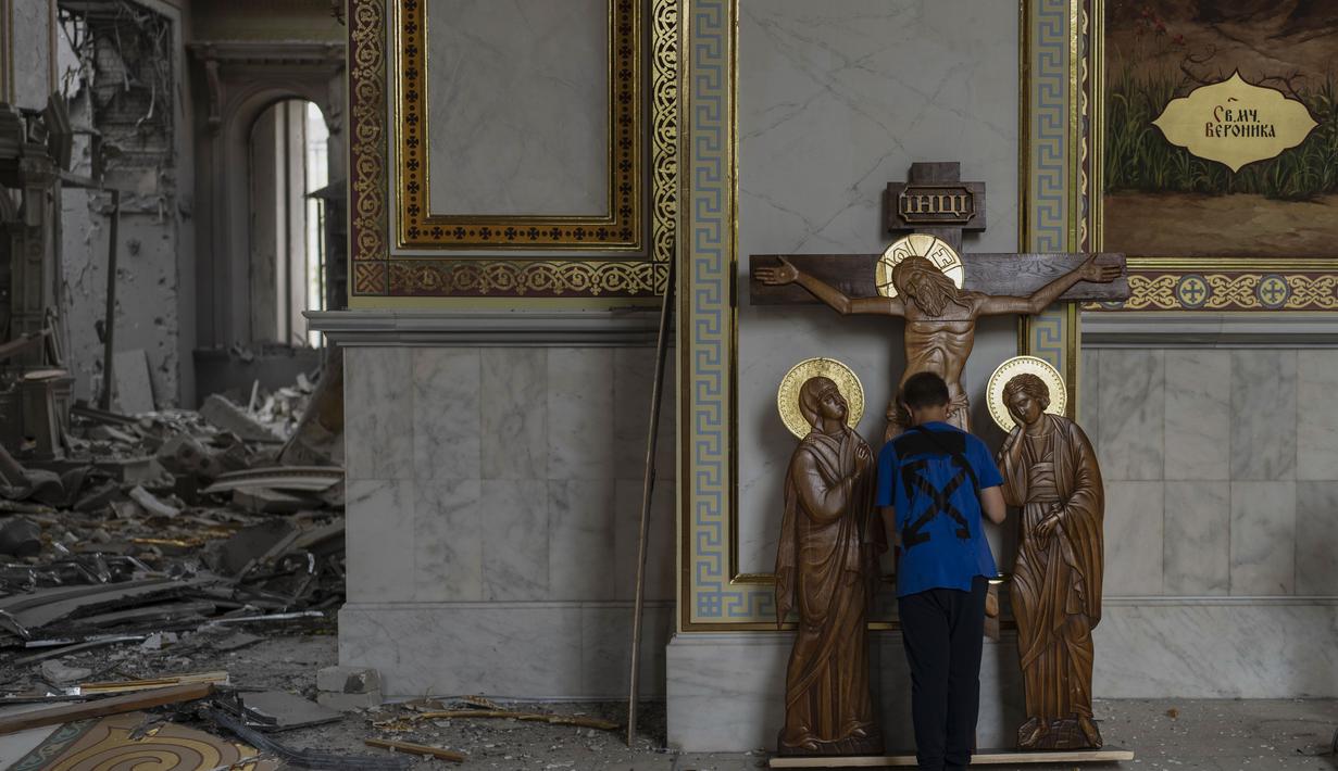 Seorang anak laki-laki mencium patung Yesus saat membantu membersihkan Katedral Transfigurasi Odesa setelah gereja rusak berat akibat serangan rudal Rusia di Odesa, Ukraina, Minggu, 23 Juli 2023. (AP Photo/Jae C. Hong)