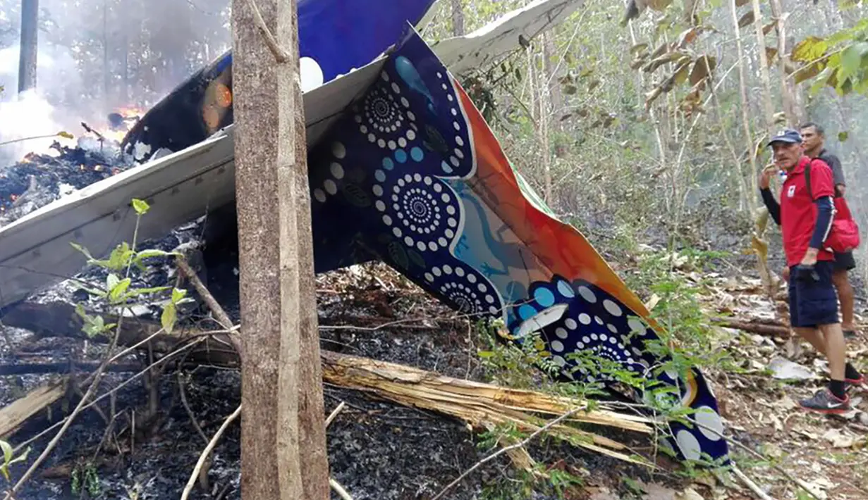Dua pria berdiri di samping ekor pesawat penumpang kecil yang jatuh di dekat Punta Islita, Kosta Rika, Minggu, (31/12). 10 warga Amerika dan 2 awak pesawat Cessna 208 Caravan tewas dalam kecelakaan tersebut. (AFP Photo/Kementerian Pertahanan Kosta Rika)