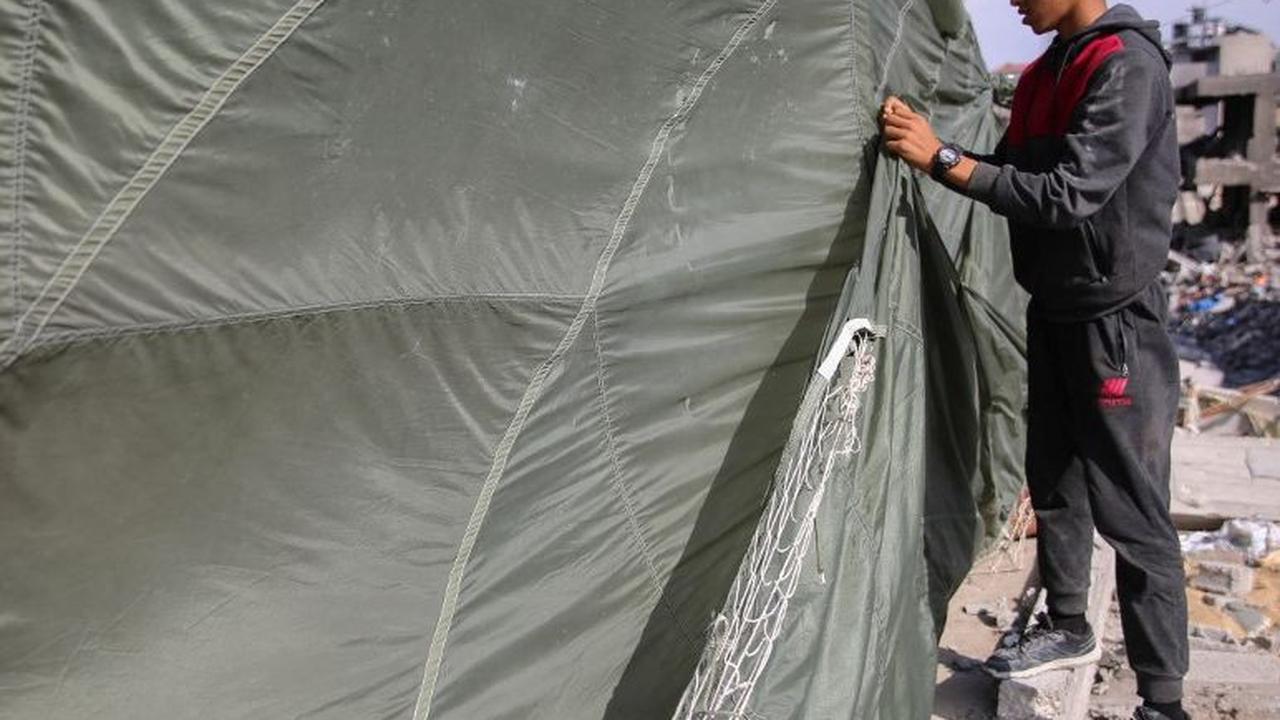 Seorang pria memperbaiki parasut militer yang dimanfaatkan sebagai tenda darurat di atas puing-puing rumahnya di Jalur Gaza, Palestina, pada Rabu (3/4/2024). Parasut tersebut sebelumnya digunakan oleh militer untuk menerjunkan bantuan kemanusiaan melalui 