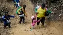 Seorang Pria dari kelompok migran membantu anak yang terjartuh dilumpur saat berjalan melintasi Celah Darien dari Kolombia ke Panama, Sabtu, (15/10/2022). Perjalanan Kelompok Imigran tersebut berharap mencapai Amerika Srikat (AS).(Fernando Vergara/AP)