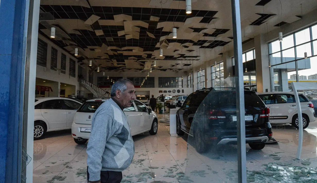 Warga berjalan melewati didinding sebuah dealer mobil yang pecah akibat serangan bom mobil di Diyarbakir, Turki bagian tenggara, Kamis (31/3). Empat personel kepolisian Turki tewas, sementara empat belas orang lainnya terluka. (Ilyas AKENGIN/AFP)