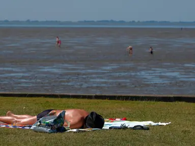 Seorang pria berjemur saat suhu mencapai 34 derajat Celcius di dekat pantai Laut Utara di Wremen, Jerman barat (24/7/2019). Peramal cuaca memprediksi suhu tertinggi di seluruh Eropa barat yang terkena gelombang panas akan mencetak rekor suhu terbaru.  (AFP Photo/Patrik Stollarz)