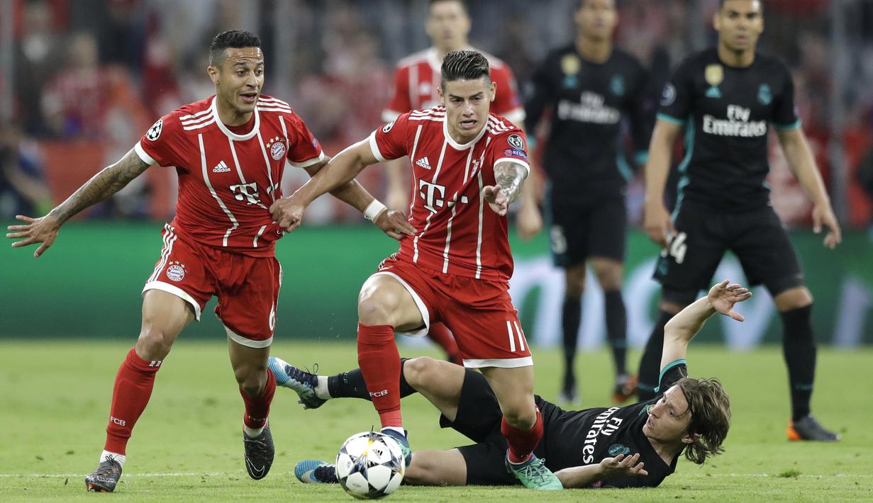 Pemain Real Madrid, Luka Modric jatuh saat berebut bola dengan pemain Bayern, Thiago dan James Rodriguez pada leg pertama semfinal Liga Champions di Allianz Arena, Munich, (25/4/2018). Real Madrid menang 2-1. (AP/Matthias Schrader)