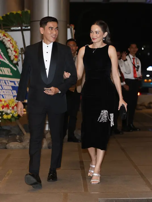 Enzy tampil beda dengan midi dress hitam tanpa lengan yang dihiasi aksen rumbai di bagian bawah, menambahkan kesan fun dan flirty. Sementara sang suami, Maulana Kasetra tampil maskulin dalam jas hitam polos, menjadi penyeimbang sempurna bagi gaya playful Enzy. [Dok/KLY/Budy Santoso].