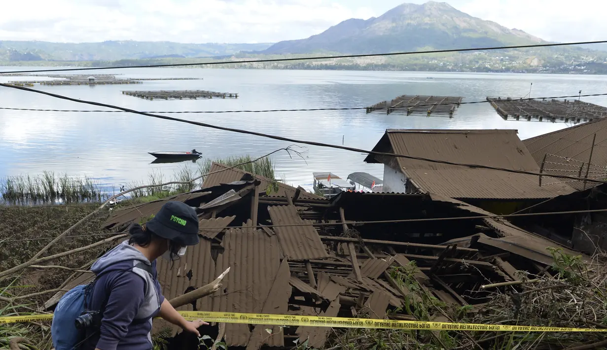 Seorang wanita berjalan melewati rumah-rumah di tepi Danau Batur yang rusak akibat tanah longsor yang dipicu gempa di Bangli, Bali, Sabtu (16/10/2021). Beberapa orang tewas dan lainnya luka-luka saat gempa berkekuatan sedang dan gempa susulan menghantam pulau itu Sabtu dini hari. (AP Photo/Dewa Raka