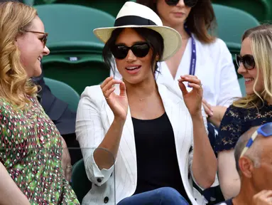 Meghan Markle (tengah) menyaksikan sahabatnya yang juga petenis AS Serena Williams melawan Kaja Juvan dari Slovakia pada babak kedua Wimbledon di All England Lawn Tennis Club, London, Kamis (4/7/2019). Meghan Markle tampil dalam balutan tank top dan jeans dengan blazer sebagai luaran (GLYN KIRK/AFP)