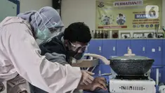 Terapis atau pengajar membimbing mahasiswa berkebutuhan khusus menyalakan kompor dalam proses pembuatan telur asin saat kelas terapi mata kuliah wirausaha di Lembaga Pendidikan dan Keterampilan Kampusnya Manusia, Kranggan, Bekasi, Jawa Barat, Kamis (3/12/2020). (merdeka.com/Iqbal S. Nugroho)
