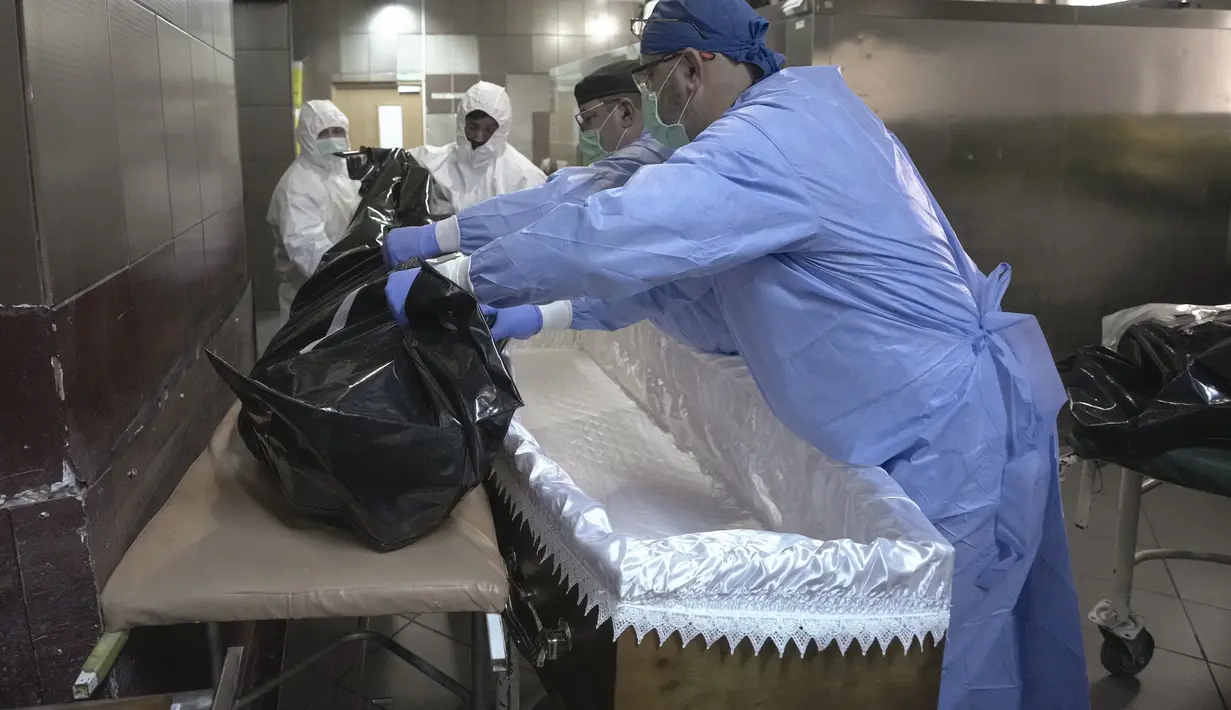 Anggota staf medis menempatkan tubuh korban COVID-19 di peti mati bersama dengan karyawan rumah duka di kamar mayat Rumah Sakit Darurat Universitas di Bucharest, Rumania, Senin (8/11/2021).  (AP Photo/Vadim Ghirda)