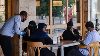 Pelayan mengenakan sarung dan masker melayani pelanggan di sebuah kafe di ibu kota Arab Saudi, Riyadh (21/6/2020). (AFP Photo/Fayez Nureldine)