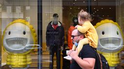Seorang ayah dan anak perempuan melewati bagian depan toko di Melbourne, Kamis (28/10/2021). Toko-toko di kota ini bersiap untuk menyambut kembali pelanggan setelah menjalani penguncian pandemi keenam. (AFP/William West)