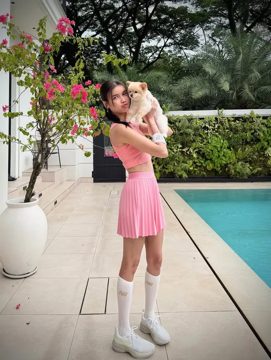 Gaya ini menciptakan kesan playful sekaligus elegan, seolah menggabungkan aura ballerina dan atlet tenis dalam satu tampilan. Rambut kepang satu sisi dan riasan natural membuatnya terlihat effortlessly chic di bawah sinar matahari.