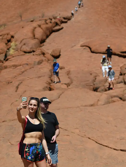 Wisatawan mendaki Uluru yang juga dikenal sebagai Batu Ayers di Taman Nasional Uluru-Kata Tjuta, utara Australia, Jumat (25/10/2019). Kawasan wisata bukit batu Uluru dipenuhi pengunjung, lantaran hari ini merupakan hari terakhir sebelum larangan pendakian diberlakukan. (SAEED KHAN / AFP)