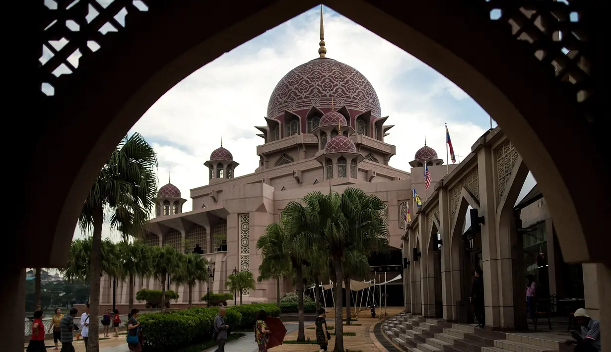 Gambar yang diambil pada 22 November 2017, menunjukkan wisatawan berjalan di sekitar Masjid Pink di kawasan Putrajaya, Malaysia. Selain warna yang unik, masjid ini juga dilengkapi dengan kubah berisikan lukisan dan kaligrafi indah. (MANAN VATSYAYANA/AFP)
