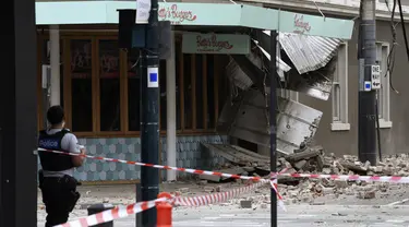 Seorang petugas polisi menutup persimpangan di mana puing-puing berserakan di jalan setelah gempa merusak sebuah bangunan di Melbourne, Rabu (22/9/2021). Gempa magnitudo 5,8 melanda dekat Melbourne dan guncangannya terasa di sejumlah wilayah di Australia pada Rabu pagi. (James Ross/AAP Image via AP)